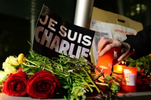 A man lights a candle next to a poster reading "Je suis Charlie" (I a